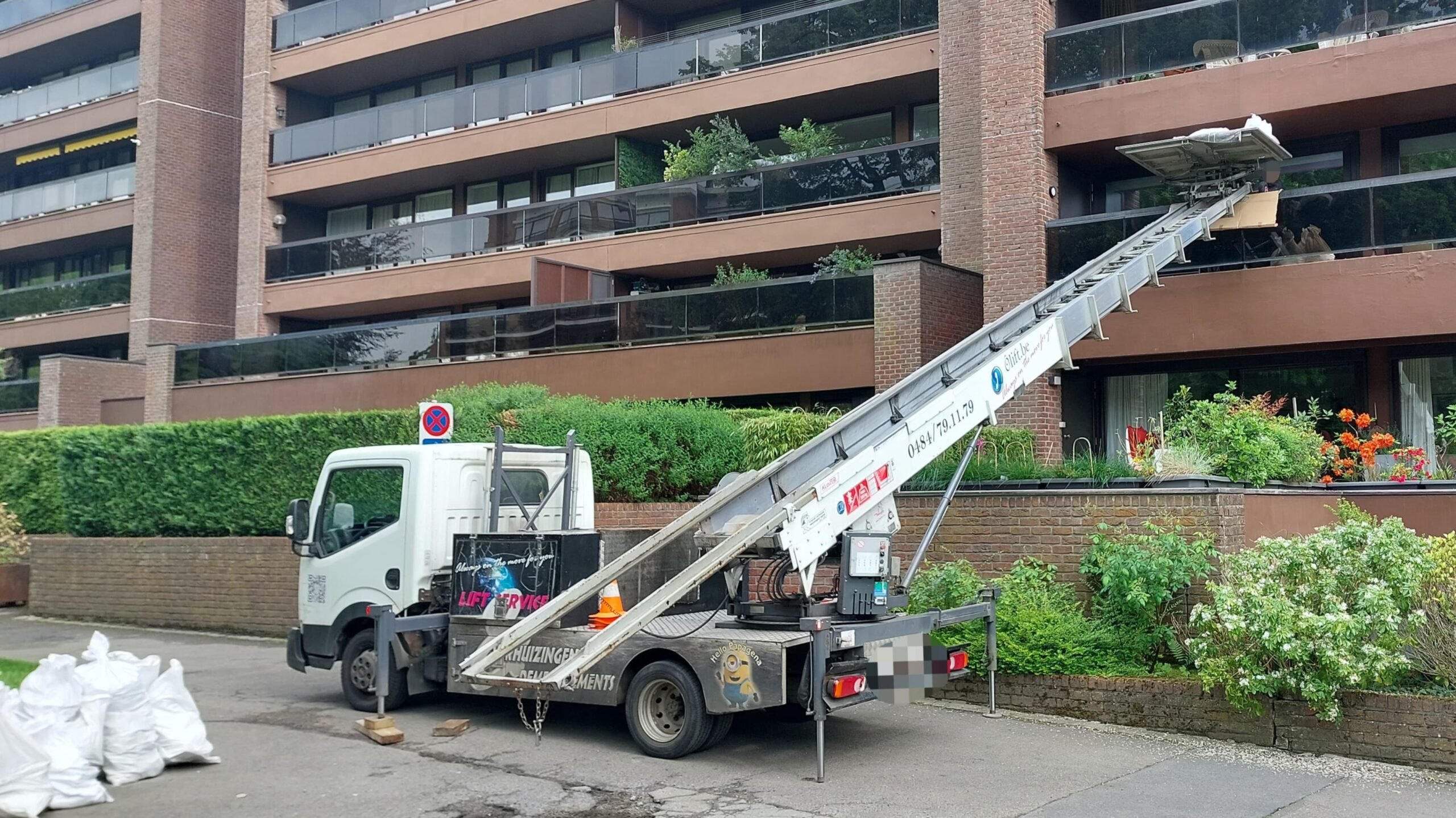 Camion-lift Ôlift.be, échelle déployée vers un immeuble à appartements moderne en briques avec balcons