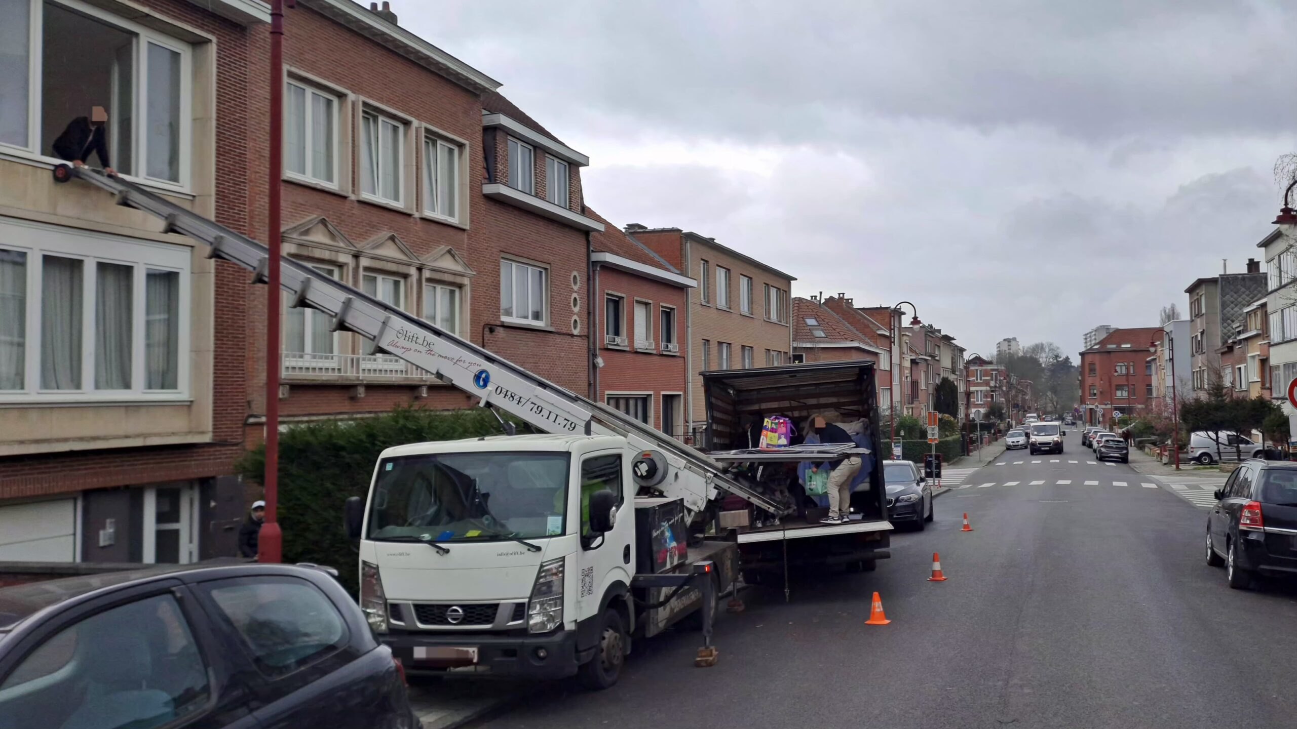 Camion-lift Ôlift.be stationné dans une rue de maisons, échelle prête à être déployée