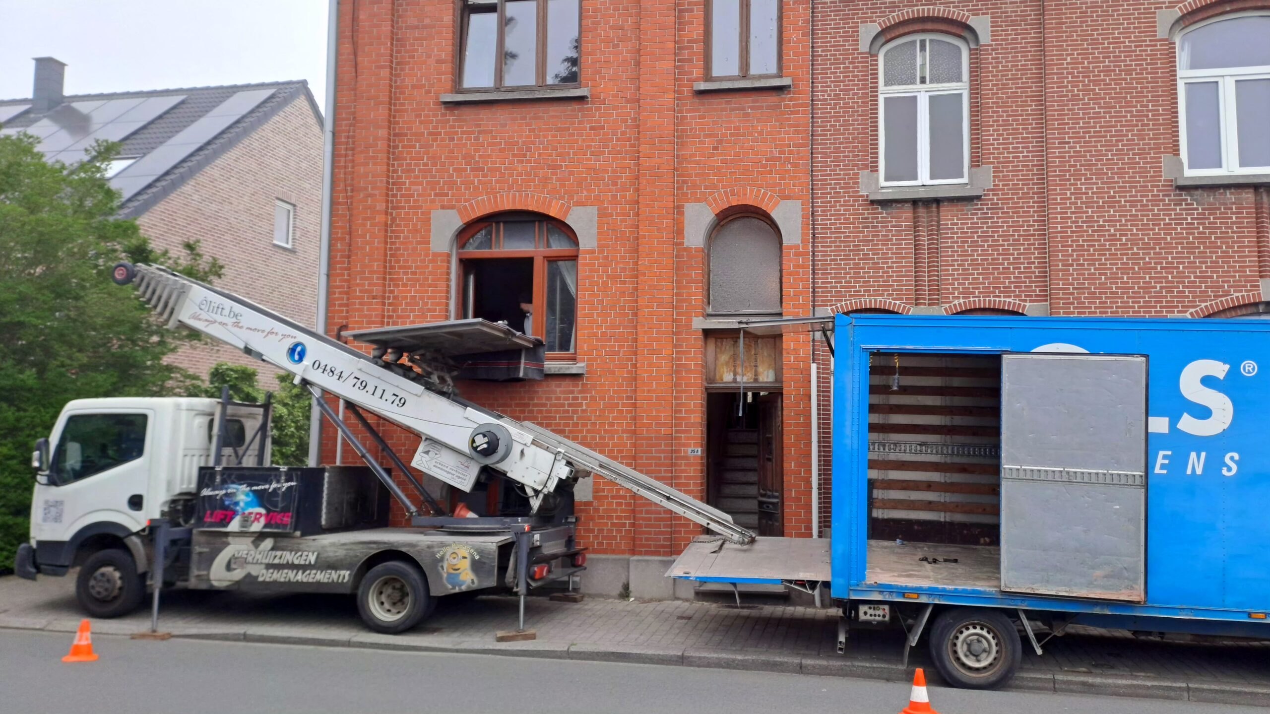 Élévateur de chantier déployé vers une maison en briques, conteneur bleu pour les gravats