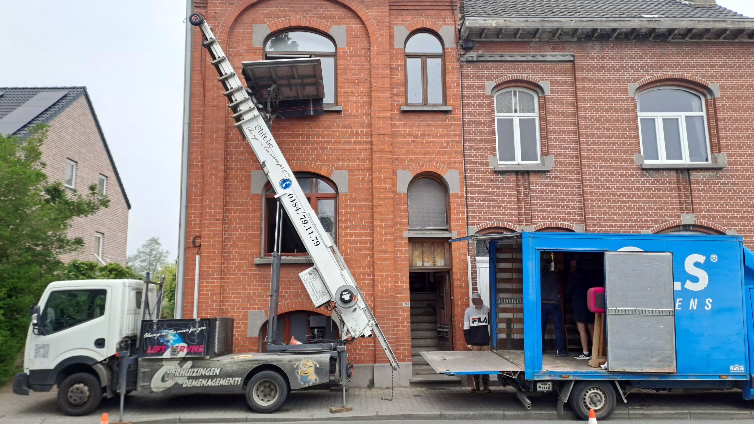 Lift monte-charge vers une façade en briques avec conteneur de chantier bleu, rénovation