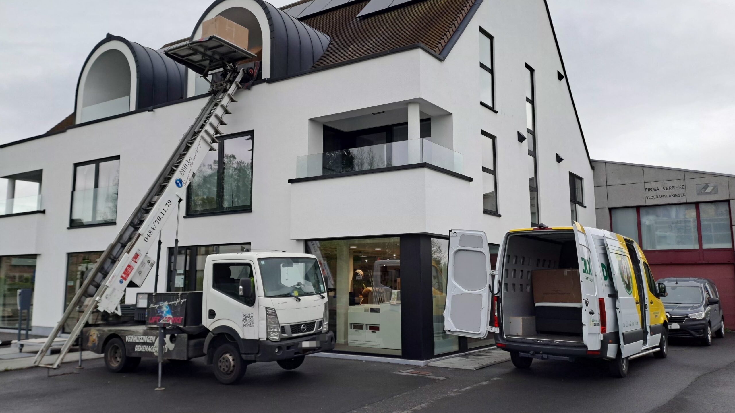 Lift de déménagement devant une maison moderne blanche, camionnette ouverte prête au chargement
